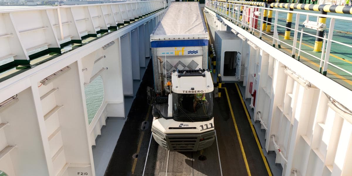 A DFDS terminal truck drives a white and blue trailer onto a DFDS RoRo vessel, as viewed from an angle above