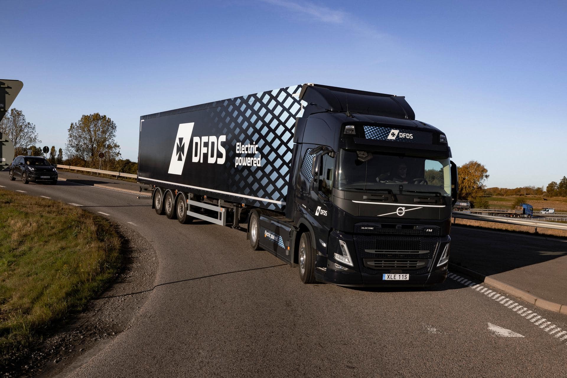 Electric truck in dark blue DFDS livery, driving on a curved part of a road, seen partly from the side