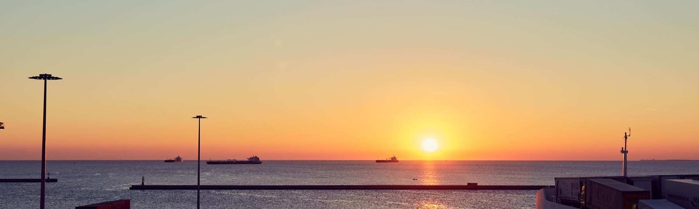 Photo of the sun setting on the sea water near a DFDS freight terminal