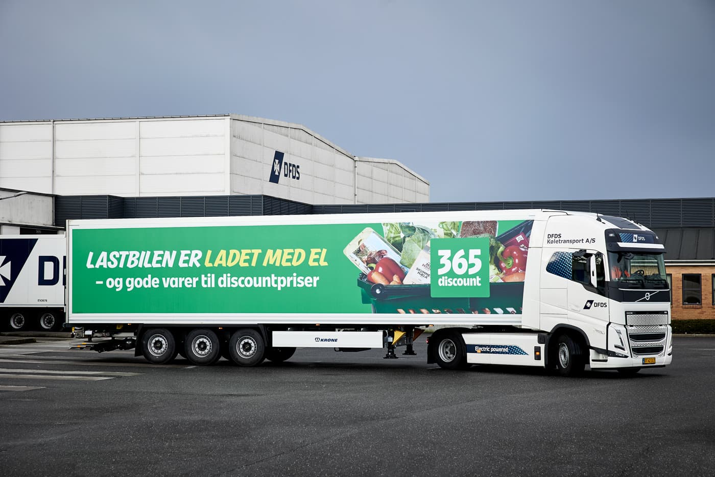 A white electrical DFDS truck with a 365Discount trailer in front of a DFDS warehouse