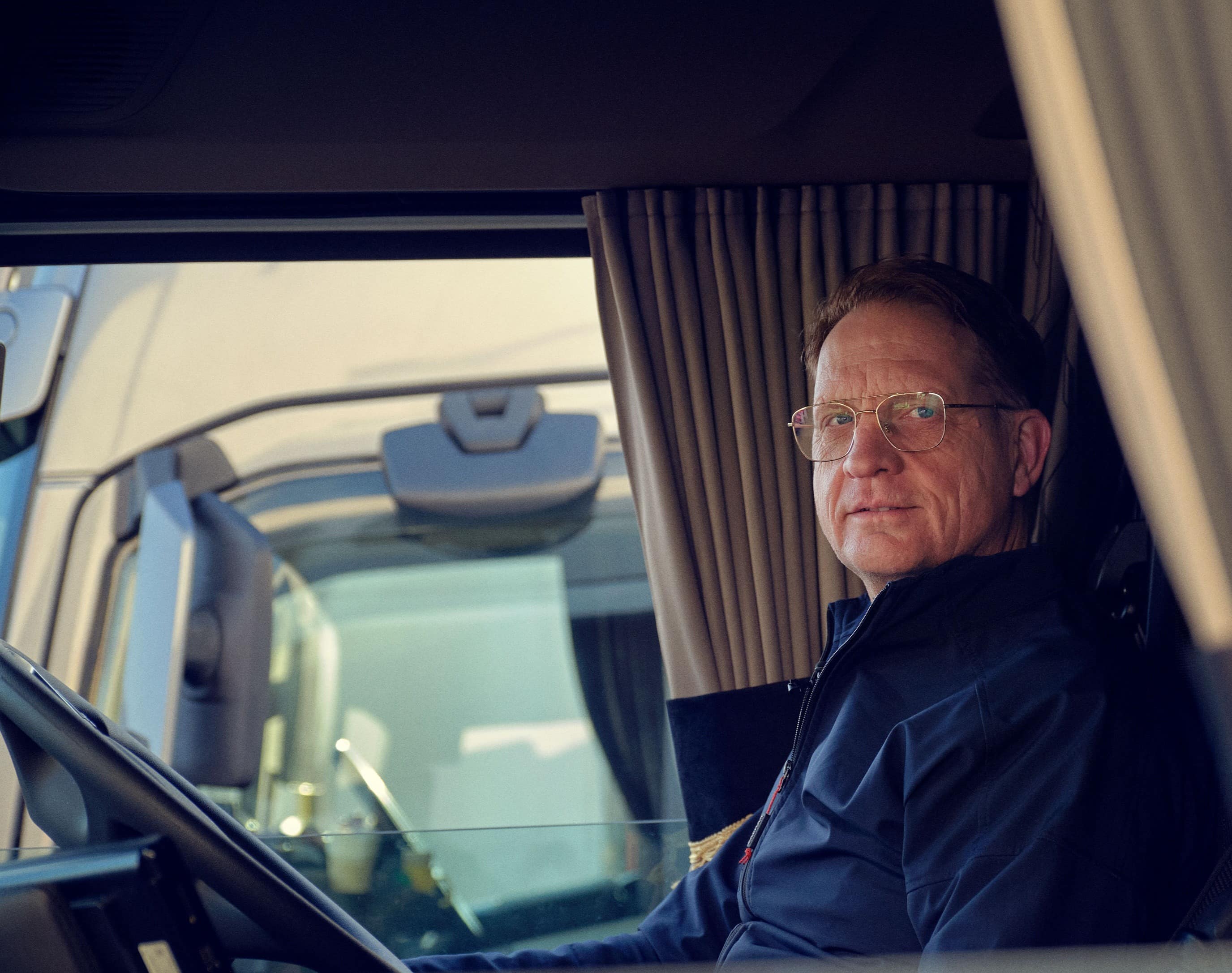 A DFDS Logistics driver sitting on the driver's seat of a truck, looking to his side
