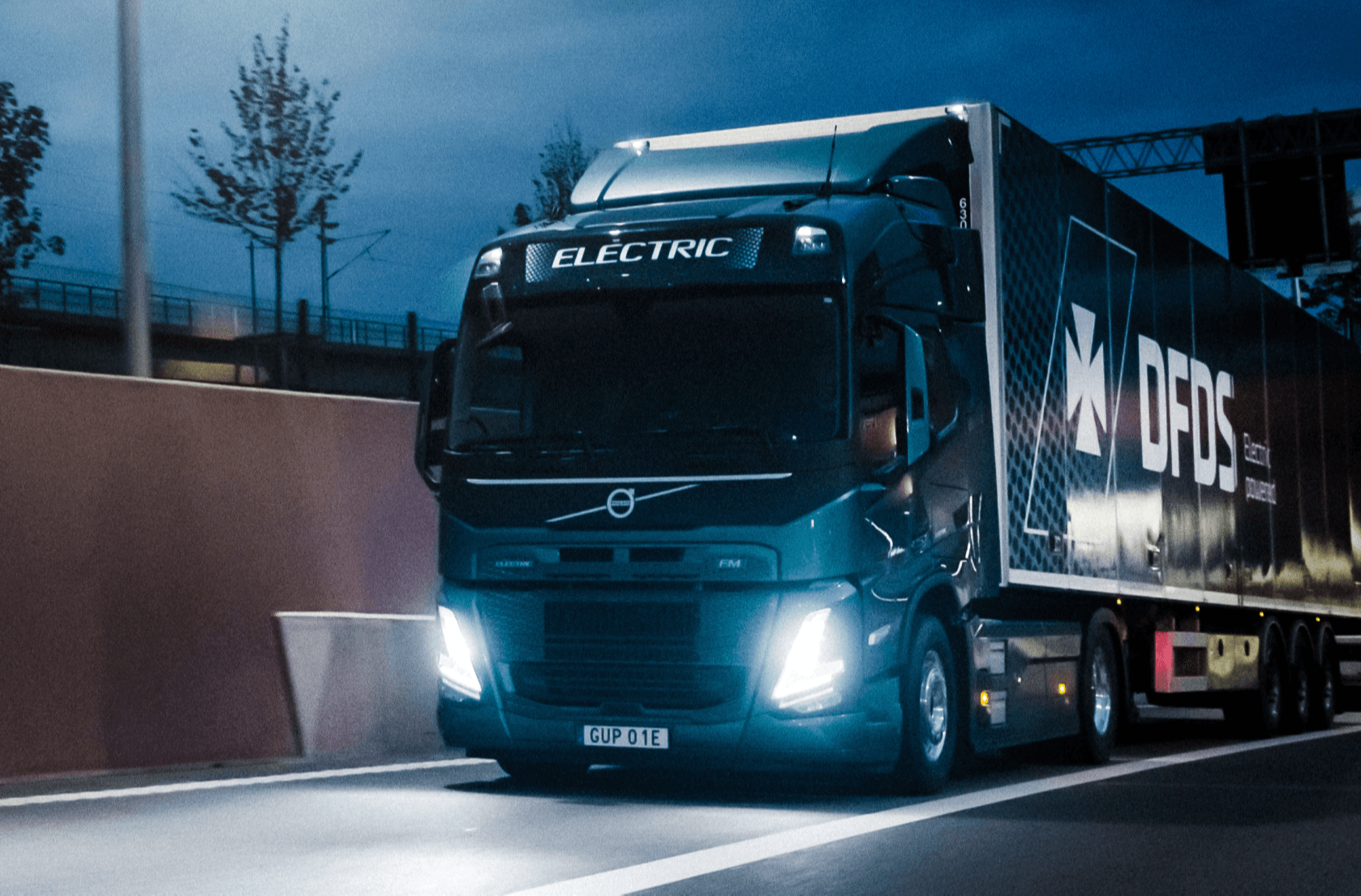 A blue, DFDS-branded electric truck drives on road at night