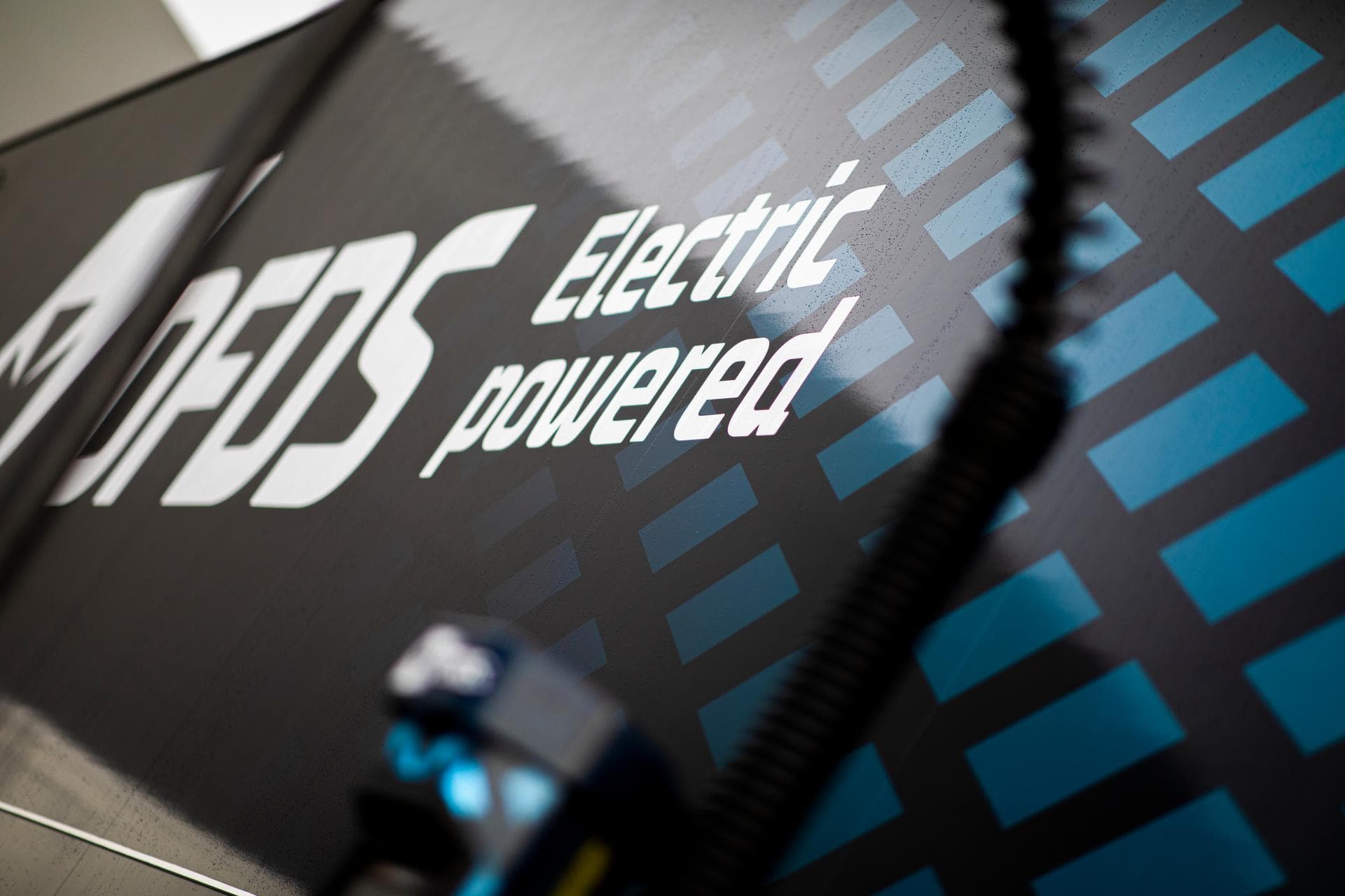 Detail of electric truck in dark blue DFDS livery, as seen from the side, with blurred detail of loading station